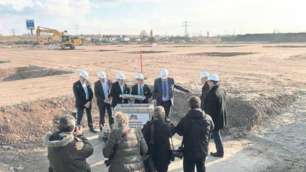 Männer, die auf Steine schauen: Noch steht auf dem Gelände des künftigen Warenverteilzentrums in Wustermark außer dem Stein nichts. Aber das soll sich schnell ändern. In zwei Jahren soll die Brache bebaut sein. 