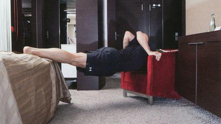 Man muss ja nicht immer alles gleich machen. Ein Mann zwischen Stuhl und Bett. Aus der Fotoreihe "TABLE ROWING" von Peter Piller.