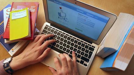 Ein junger Mann ruft zwischen Schul- und Lehrbüchern auf einem Laptop die Internetseite von Facebook auf.