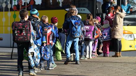 Schüler steigen vor einer Schule in einen Schulbus ein.
