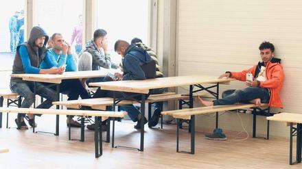 Flüchtlinge sitzen im Aufenthaltsraum einer Unterkunft an Tischen.
