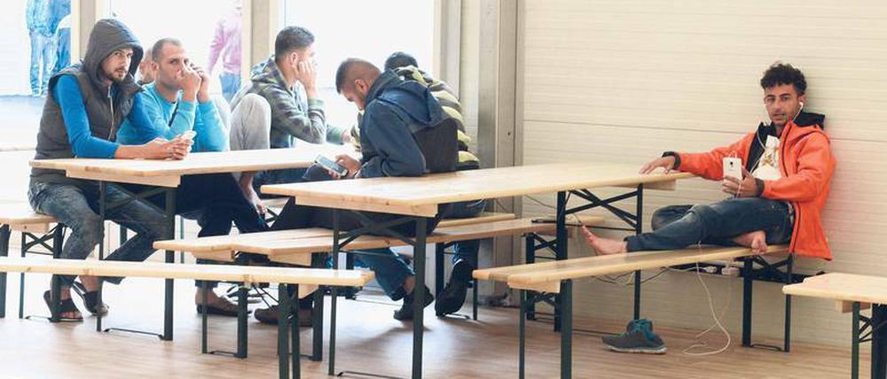 Flüchtlinge sitzen im Aufenthaltsraum einer Unterkunft an Tischen.