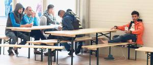 Flüchtlinge sitzen im Aufenthaltsraum einer Unterkunft an Tischen.