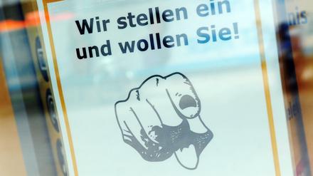 Ein Zettel mit der Aufschrift "Wir stellen ein und wollen Sie!" hängt in einem Schaufenster.