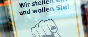 Ein Zettel mit der Aufschrift "Wir stellen ein und wollen Sie!" hängt in einem Schaufenster.