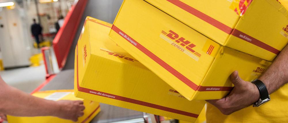 Mitarbeiter eines Logistikunternehmens DHL legen am Pakete auf ein Laufband.