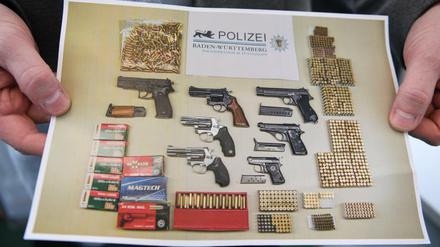 Ein Polizist hält ein Foto in der Hand, das das Ergebnis einer Aktion gegen illegalen Waffenhandel zeigt.