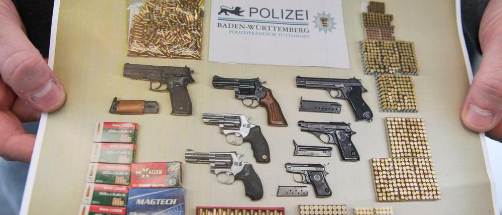 Ein Polizist hält ein Foto in der Hand, das das Ergebnis einer Aktion gegen illegalen Waffenhandel zeigt.