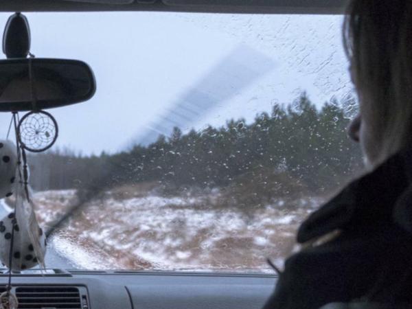 Blick von der Hinterbank in den Frontbereich eines Auto, das auf einer verlassenen Landstraße fährt. Neben der Fahrerin, die nur schemenhaft erkennbar ist, sitzt rechts ein Mann.