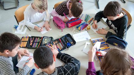 Schülerinnen und Schüler sitzen an einem Gruppenarbeitstisch in ihrer Klasse zusammen.