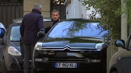 Das Video-Standbild zeigt Nicolas Sarkozy (r), früherer Staatspräsident von Frankreich, als er sein Pariser Zuhause verlässt. 