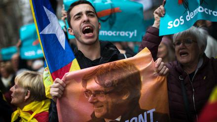 Spanien, Barcelona: Ein Demonstrant, der für die Unabhängigkeit Kataloniens ist, hält ein Poster mit einem Bild des abgesetzten ehemaligen Präsidenten der spanischen Region Katalonien Puigdemont. Der katalanische Ex-Regionalpräsident Puigdemont ist am 25.03.2018 nach der Einreise aus Dänemark in Deutschland festgenommen worden.