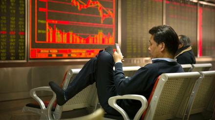 Der Freitag nach Trumps Strafzoll-Beschlüssen blickt ein chinesischer Investor auf sein Smartphone, während er in einem Brokerhaus die Börsenpreise verfolgt.