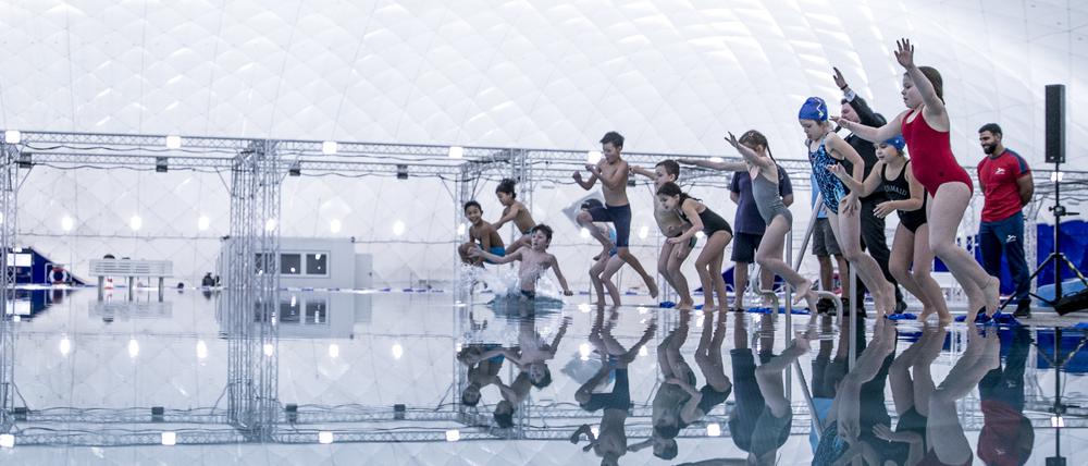 04.12.2019, Berlin: Kinder springen in das Wasserbecken bei der offiziellen Eröffnung der Schwimmbad-Traglufthalle. Die Schwimmhalle ist mit einer Grundfläche von 60 mal 68 Metern die größte Schwimmbad-Traglufthalle Deutschlands. Durch die Überdachung der beiden Freibäder kommen für die Wintermonate 2072 Quadratmetern Wasserfläche dazu. Foto: Carsten Koall/dpa +++ dpa-Bildfunk +++