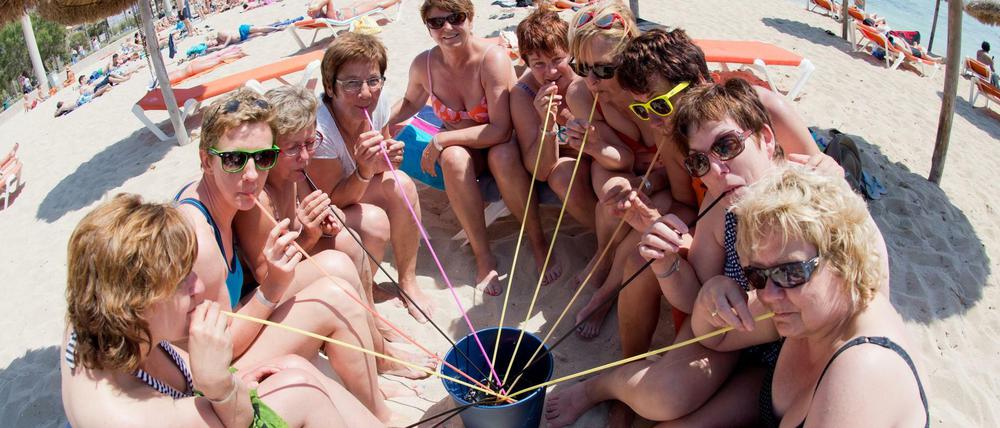 Deutsche Touristinnen trinken aus einem Eimer am Strand auf Mallorca.