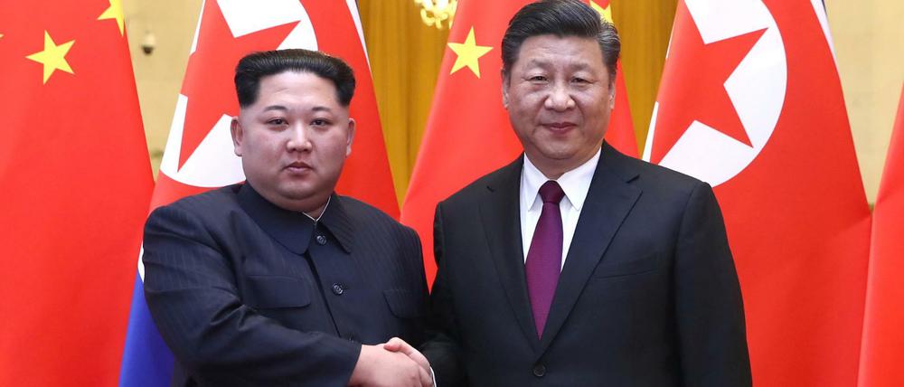 Nordkoreas Machthaber Kim Jong Un und Chinas Präsident Xi Jinping stehen nebeneinander und geben sich die Hand.