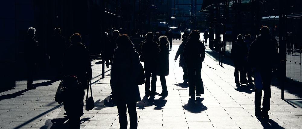 Im Gegenlicht zeichnen sich Passanten auf einem Gehweg in Dresden als dunkle Silhouetten ab.