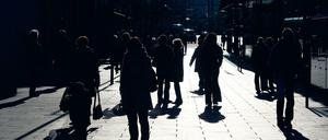 Im Gegenlicht zeichnen sich Passanten auf einem Gehweg in Dresden als dunkle Silhouetten ab.