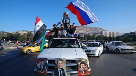 Unterstützer der syrischen Regierung in Damaskus schwenken eine syrische, eine russische und eine iranische Fahne.