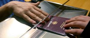 Ein Deutscher Pass wird bei einer Passkontrolle unter einer Scheibe durchgereicht. 