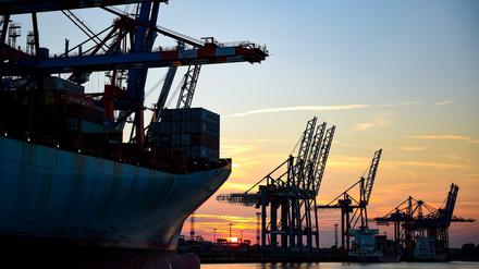 Die Sonne geht am im Hamburger Hafen hinter Kränen zur Containerverladung unter. 