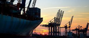 Die Sonne geht am im Hamburger Hafen hinter Kränen zur Containerverladung unter.