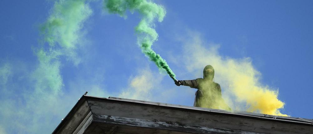 Ein Aktivist steht auf einem Hausdach und hält am Rande der Demonstration Bengalische Feuer in die Höhe.