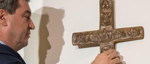Markus Söder, Bayerischer Ministerpräsident (CSU), hängt ein Kreuz im Eingangsbereich der bayerischen Staatskanzlei auf. 