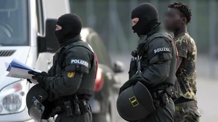 In der Landeserstaufnahmeeinrichtung für Flüchtlinge wird ein Mann von maskierten Polizisten eskortiert.
