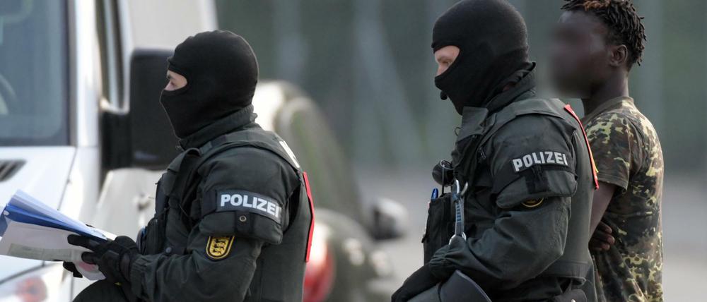 In der Landeserstaufnahmeeinrichtung für Flüchtlinge wird ein Mann von maskierten Polizisten eskortiert.