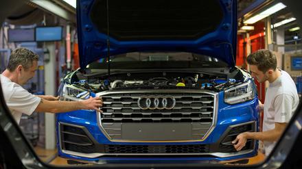 Zwei Fertigungsmechaniker bringen an einem Fließband im Audi-Werk das Frontende an einem Audi an.