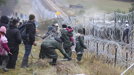 dpatopbilder - 08.11.2021, Belarus, Grodno: Migranten stoßen an der weißrussisch-polnischen Grenze einen Zaun um, während die Polizei hinter einem Stacheldrahtzaun steht. Mehrere Hundert Migranten haben sich nach Angaben der Behörden in Belarus zu Fuß auf den Weg zur Grenze zum EU-Nachbarland Polen gemacht. Foto: Leonid Shcheglov/BelTA/AP/dpa +++ dpa-Bildfunk +++