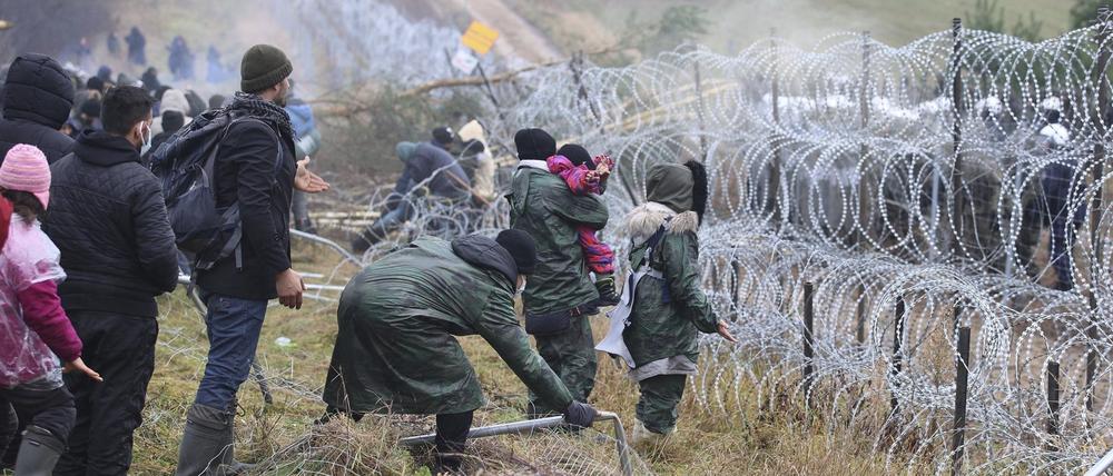 dpatopbilder - 08.11.2021, Belarus, Grodno: Migranten stoßen an der weißrussisch-polnischen Grenze einen Zaun um, während die Polizei hinter einem Stacheldrahtzaun steht. Mehrere Hundert Migranten haben sich nach Angaben der Behörden in Belarus zu Fuß auf den Weg zur Grenze zum EU-Nachbarland Polen gemacht. Foto: Leonid Shcheglov/BelTA/AP/dpa +++ dpa-Bildfunk +++