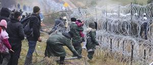 dpatopbilder - 08.11.2021, Belarus, Grodno: Migranten stoßen an der weißrussisch-polnischen Grenze einen Zaun um, während die Polizei hinter einem Stacheldrahtzaun steht. Mehrere Hundert Migranten haben sich nach Angaben der Behörden in Belarus zu Fuß auf den Weg zur Grenze zum EU-Nachbarland Polen gemacht. Foto: Leonid Shcheglov/BelTA/AP/dpa +++ dpa-Bildfunk +++