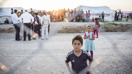 Kinder stehen hinter dem Zaun eines Flüchtlingslagers im Irak.