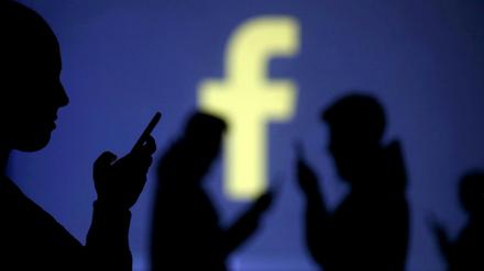 Smartphone-Benutzer vor einer Projektion des Facebook-Logos.