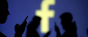 Smartphone-Benutzer vor einer Projektion des Facebook-Logos.