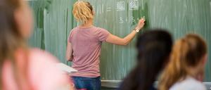 Eine Lehrerin steht vor der Klasse und schreibt eine einfache Gleichung an die Tafel.