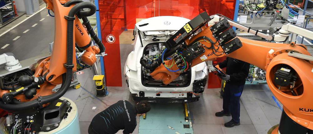 Mitarbeiter von Mercedes-Benz überwachen im Werk in Bremen, wie ein Roboter in das C-Klasse Hybrid Modell eine Batterie einsetzt.