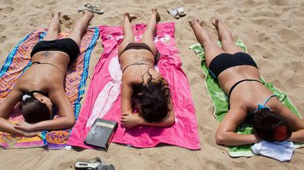 Frauen liegen am Strand des Helenesees in der Sonne. 