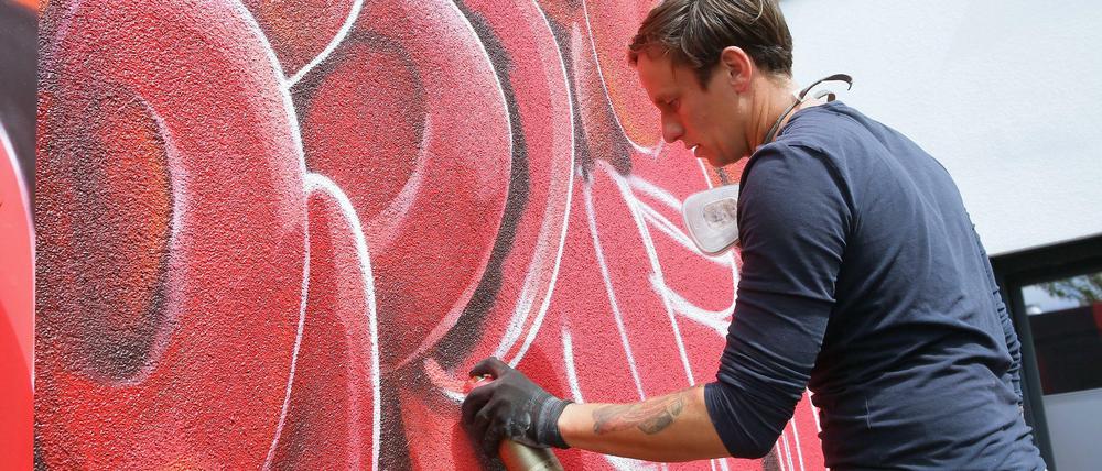 Graffiti-Künstler sprüht rot auf Wand.