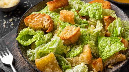 Classic Caesar salad with crisp homemade croutons, parmesan cheese and caesar dressing in a plate on black background
