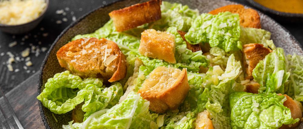 Classic Caesar salad with crisp homemade croutons, parmesan cheese and caesar dressing in a plate on black background