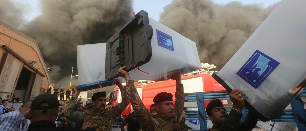Sicherheitskräfte tragen Wahlurnen aus dem brennenden Gebäude.