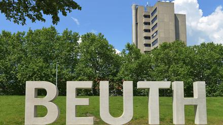 In Beton gegossene Buchstaben des Wortes Beuth stehen auf einer Wiese, im Hintergrund ist ein Hochhaus zu sehen.