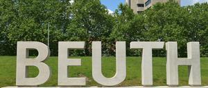 In Beton gegossene Buchstaben des Wortes Beuth stehen auf einer Wiese, im Hintergrund ist ein Hochhaus zu sehen.