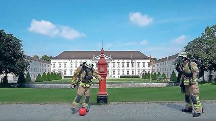 Berliner Feuerwehrleute kicken einen roten Ball vor dem Schloss Bellevue.