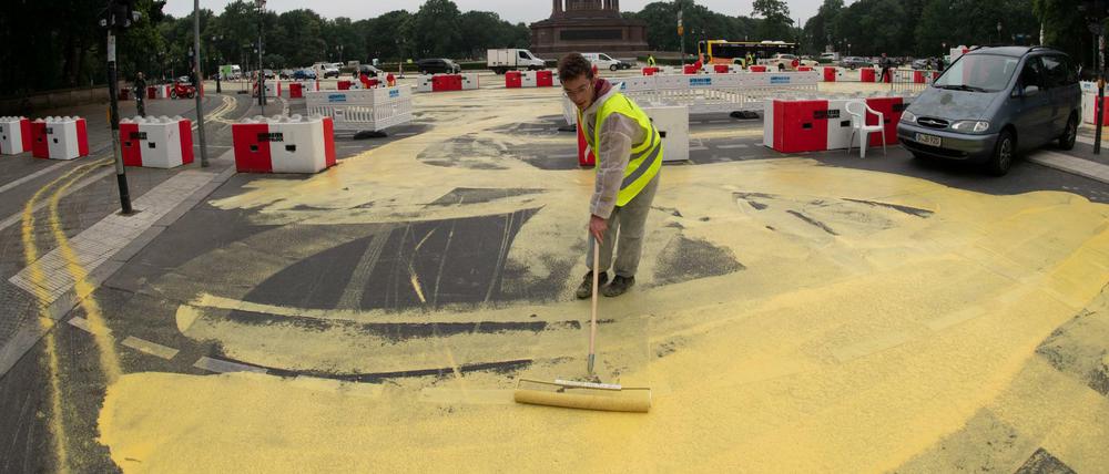 Ein Greenpeace-Aktivist schmiert Farbe aus Spinellgelb auf die Straße am Großen Stern.