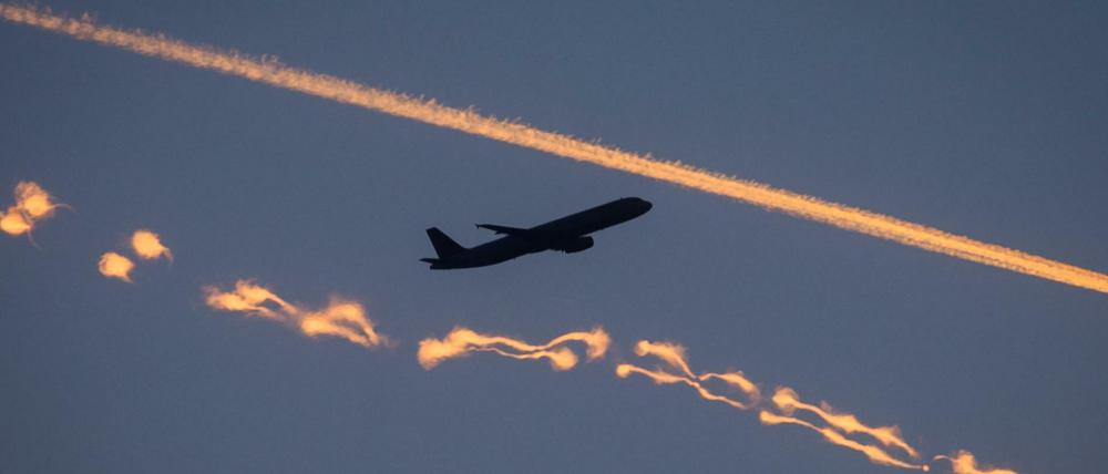 Ein Passagierflugzeug zwischen zwei von der Sonne gefärbten Kondensstreifen.