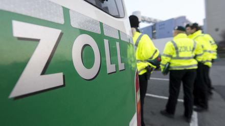 Zollbeamte vor ihrem Dienstfahrzeug auf einem Parkplatz.